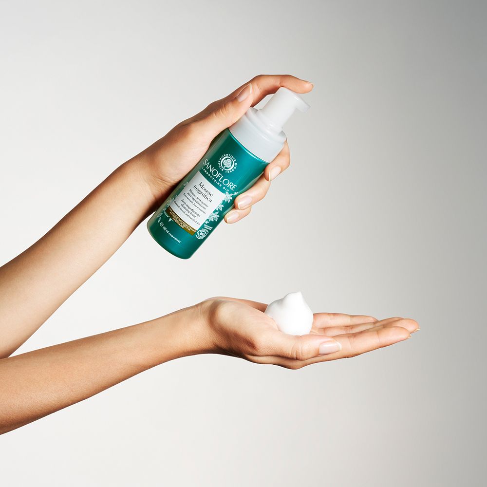 Hände halten eine Flasche und Schaum. Flasche: Sanoflore Mousse Magnifica.