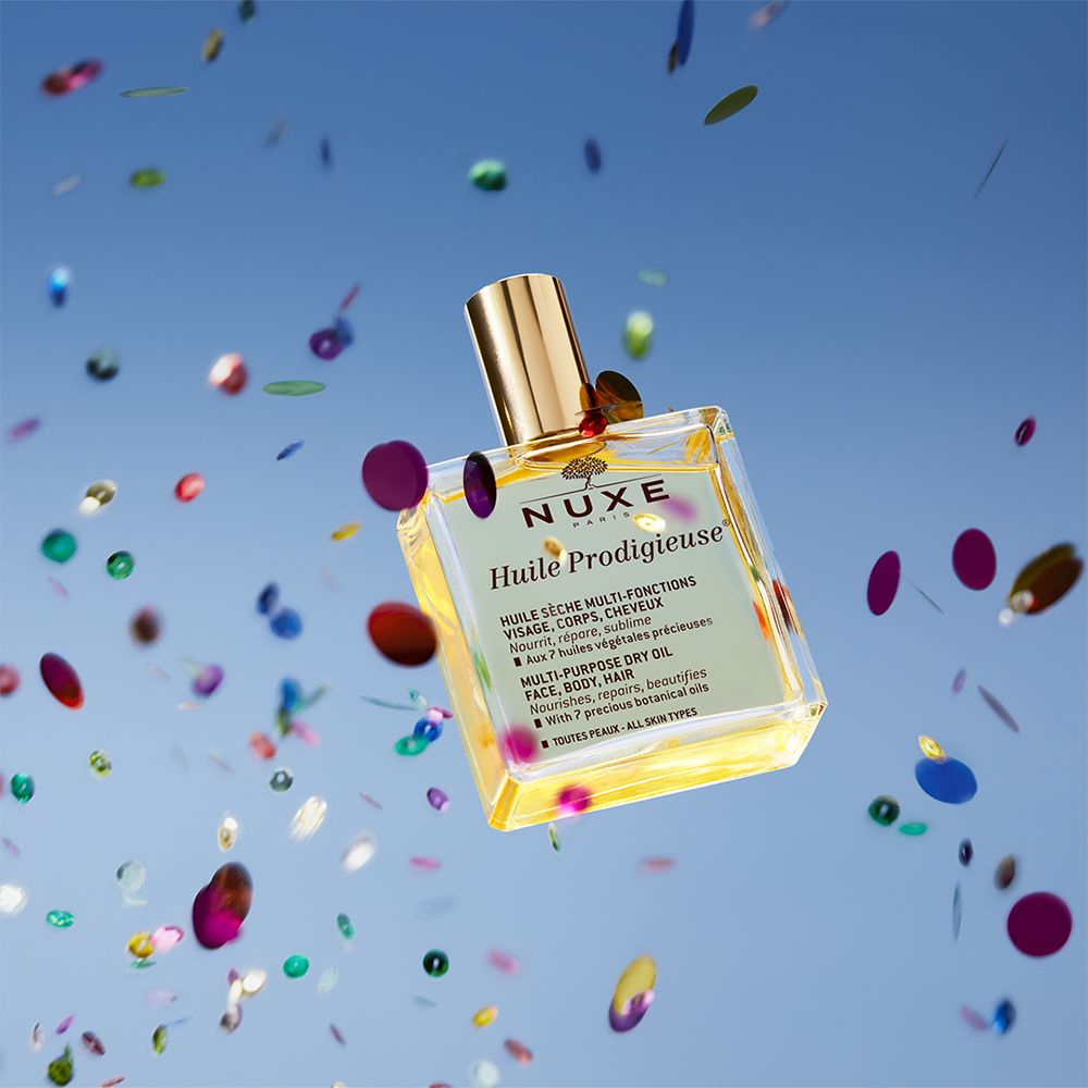 Flacon Nuxe Huile Prodigieuse, carré, bouchon doré, liquide jaune, confettis.