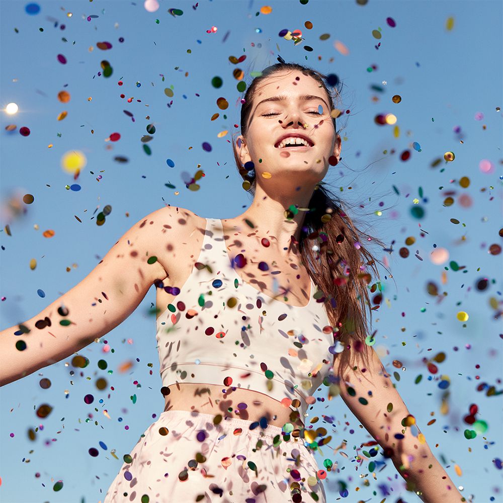Femme aux bras ouverts, confettis tombant d'en haut, ciel bleu.