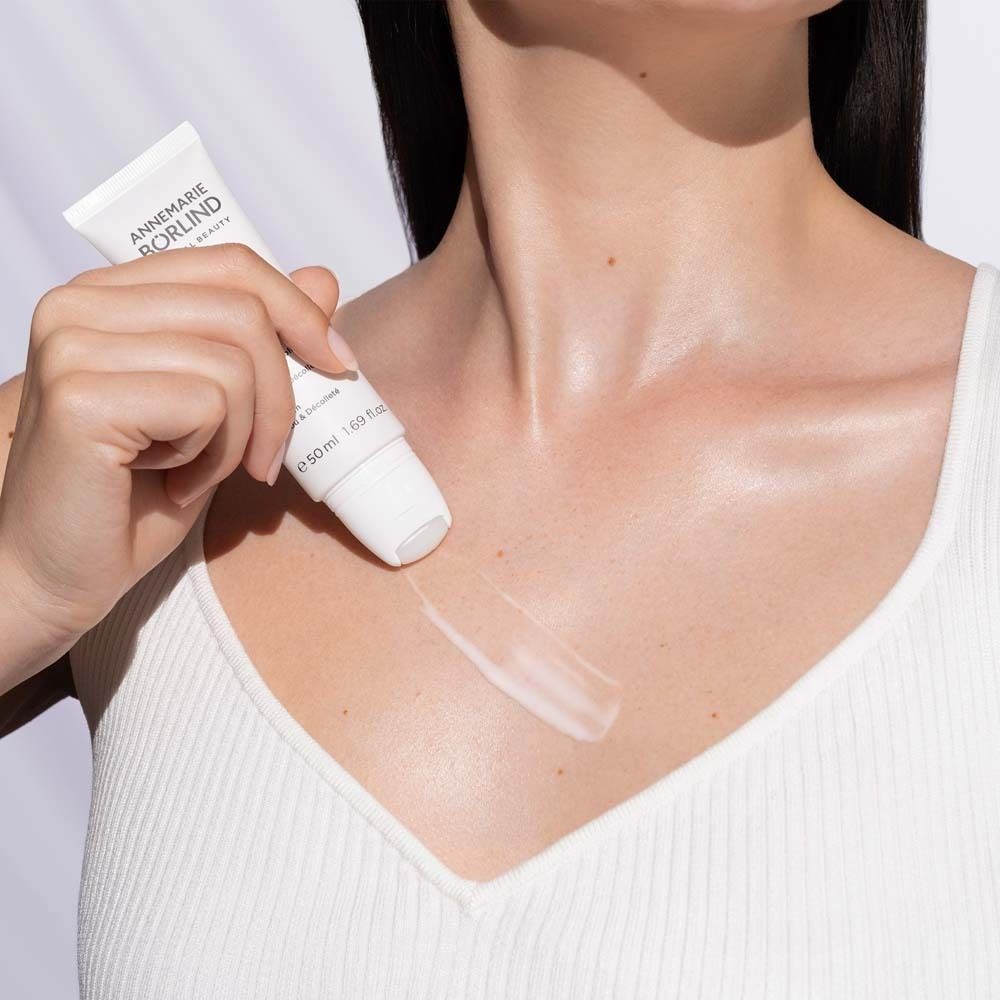 Femme portant un haut blanc. Elle tient un tube et applique du sérum sur son cou. Marque : ANNEMARIE BÖRLIND.