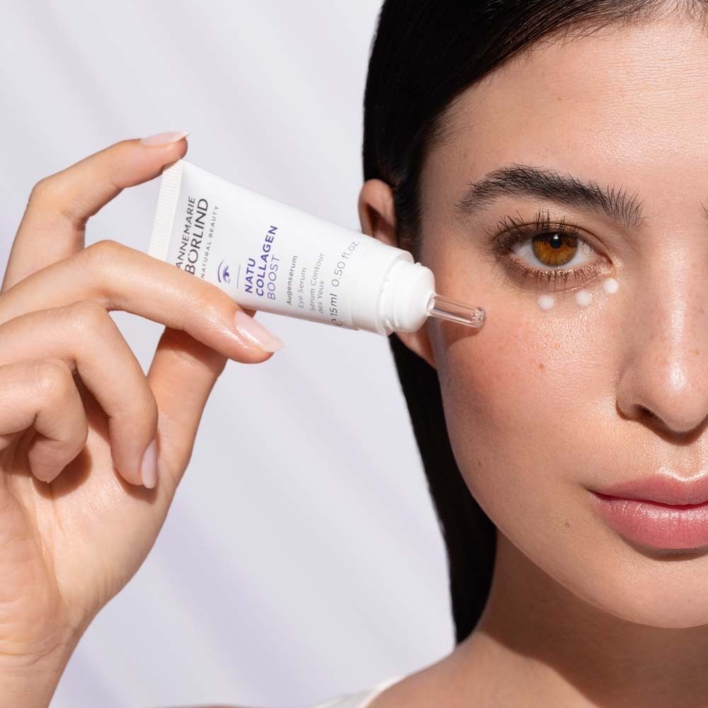 Femme appliquant un sérum pour les yeux. Tube blanc avec texte violet. Marque : ANNEMARIE BÖRLIND. Avec applicateur.