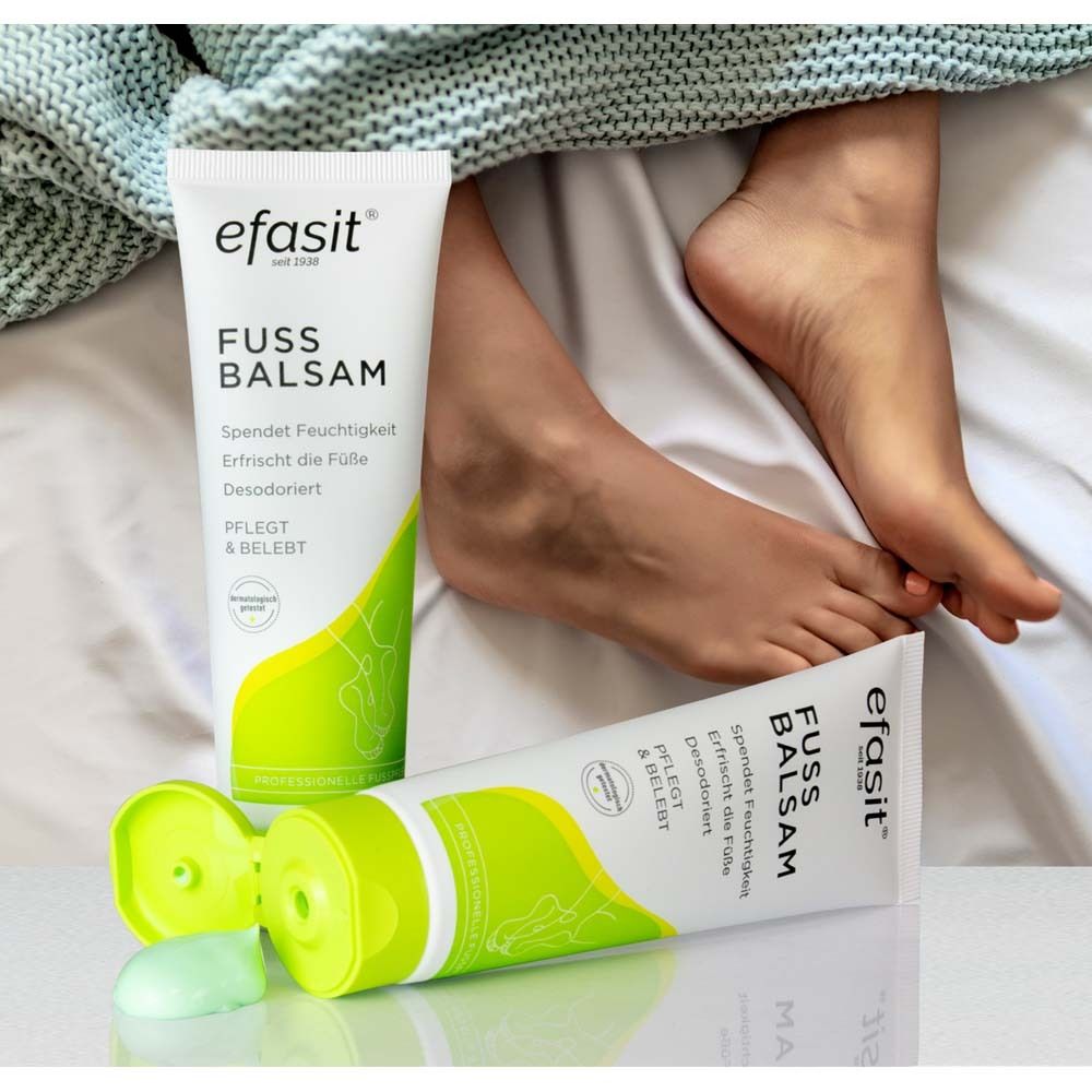 Zwei efasit® FUSS BALSAM Tuben. Eine geöffnet, eine geschlossen. Füße auf Bettwäsche. Grüner Deckel.