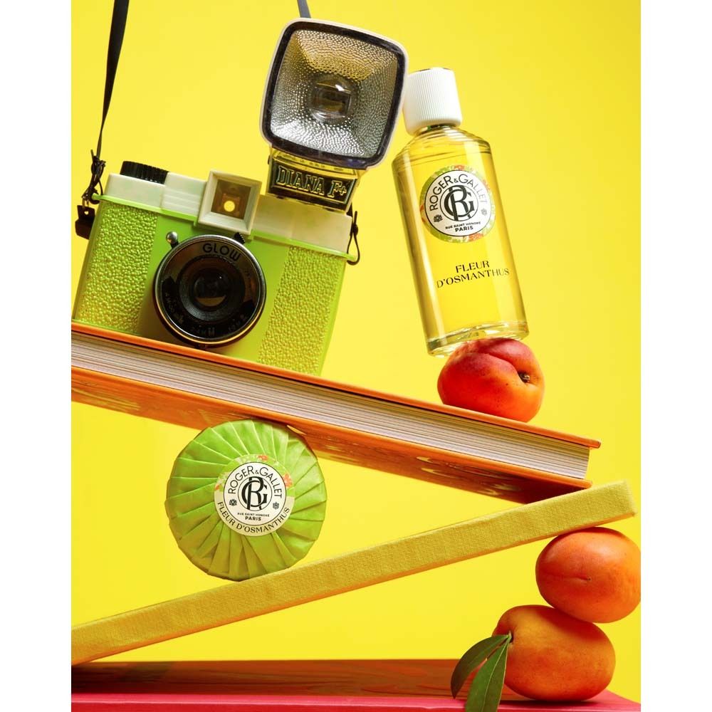 Scène jaune avec appareil photo, livres, pêches et savon. Flacon: Fleur d'Osmanthus.