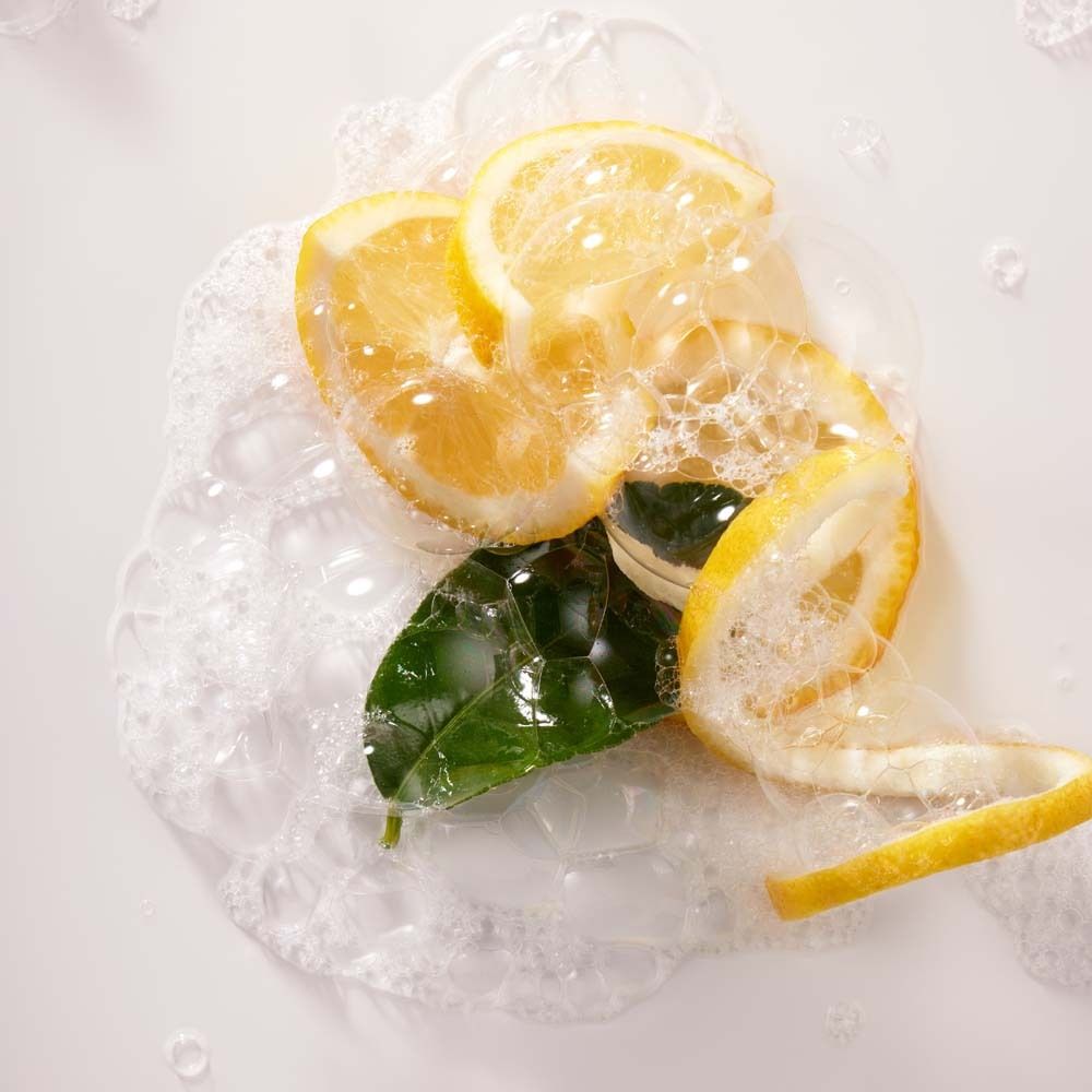 Zitronenscheiben, Blätter und Schalen in Seifenschaum. Nahaufnahme auf weißem Hintergrund.