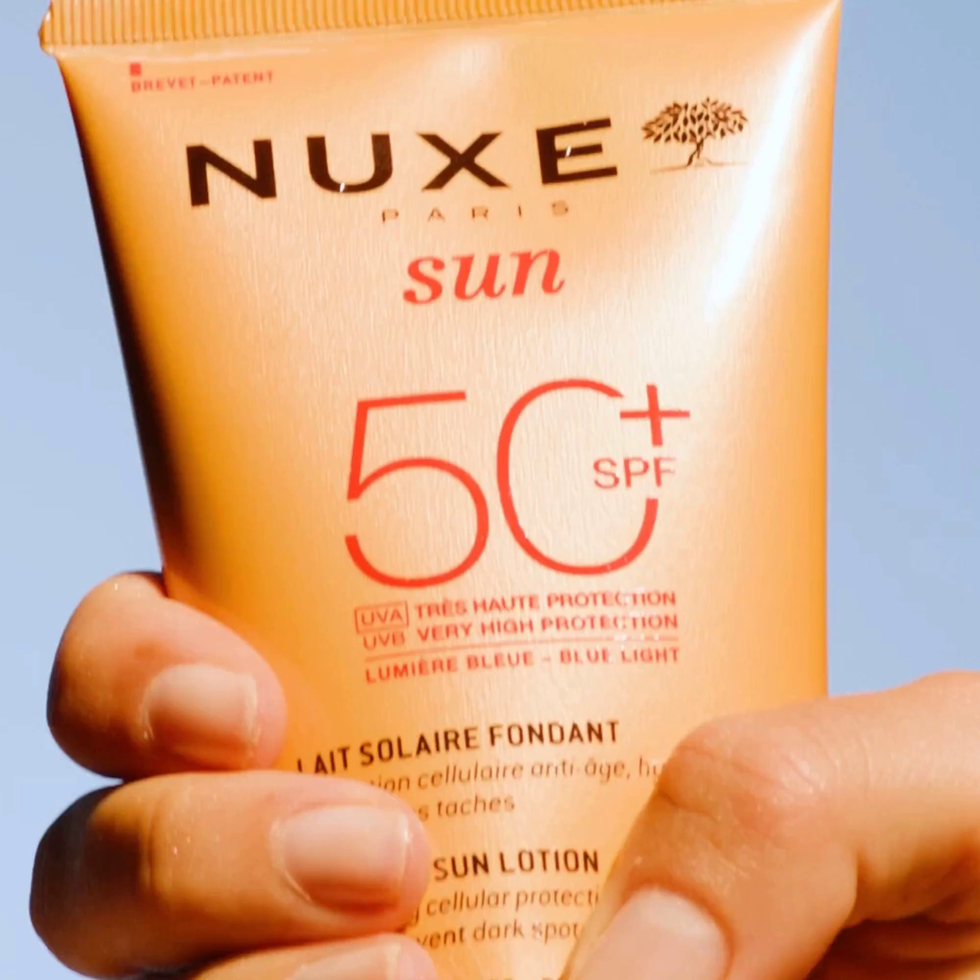 Main tenant un tube orange NUXE Sun, SPF 50. Lait Solaire Fondant.