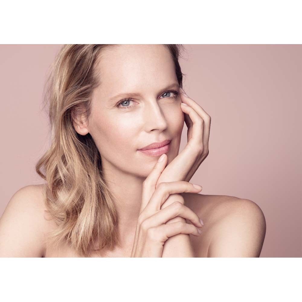 Porträt einer Frau mit blonden Haaren. Sie berührt sanft ihr Gesicht mit der Hand. Rosa Hintergrund.