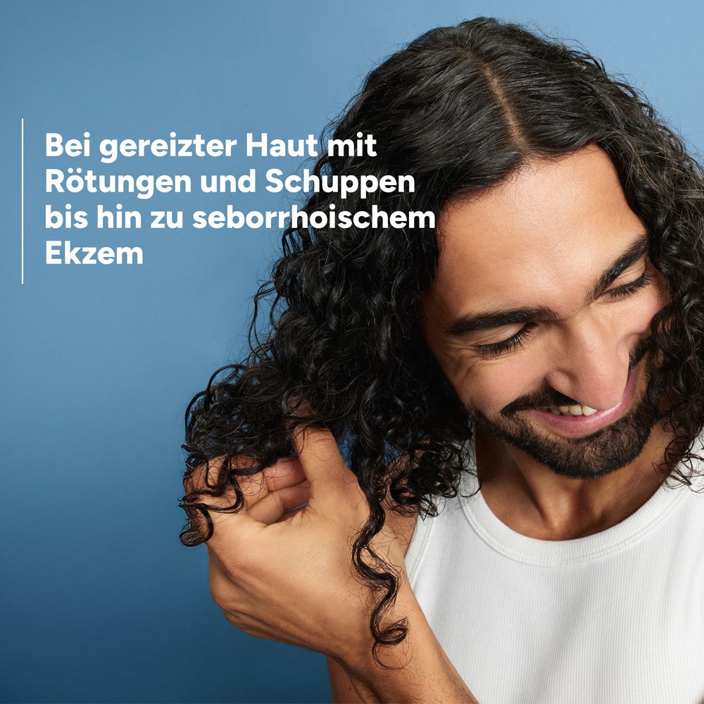 Mann mit lockigem Haar kratzt sich am Kopf, Text: Bei gereizter Haut mit Rötungen und Schuppen bis hin zu seborrhoischem Ekzem.