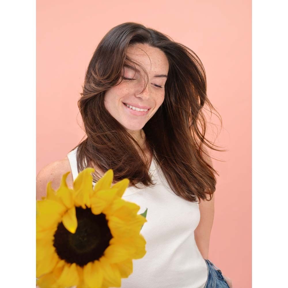 Frau mit braunem Haar und Sonnenblume. Sie lächelt und hält die Blume vor sich.