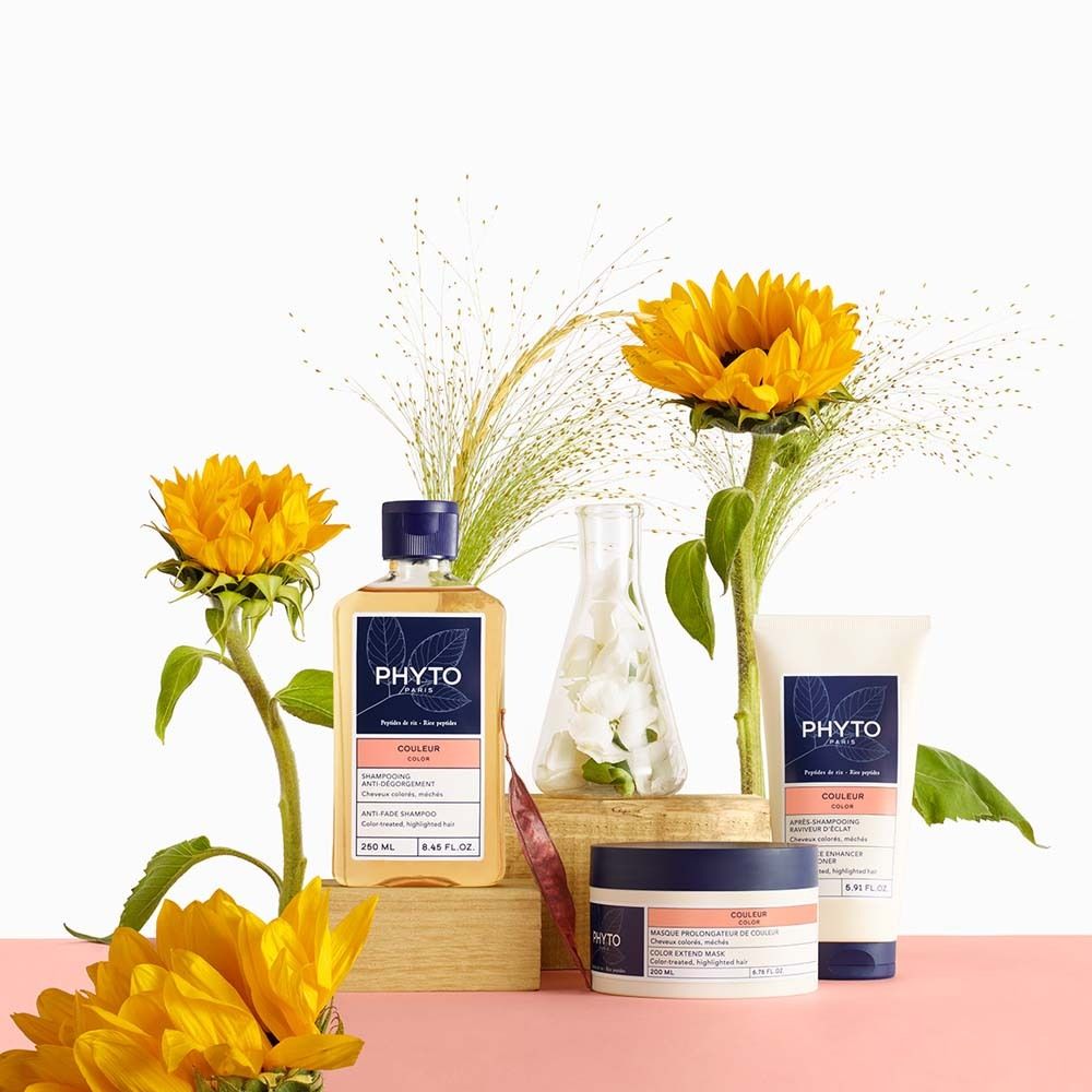 Produkt-Arrangement mit Sonnenblumen. Flasche, Tube und Tiegel mit Etiketten. Text: PHYTO PARIS, COULEUR COLOR. Auf rosa Untergrund.