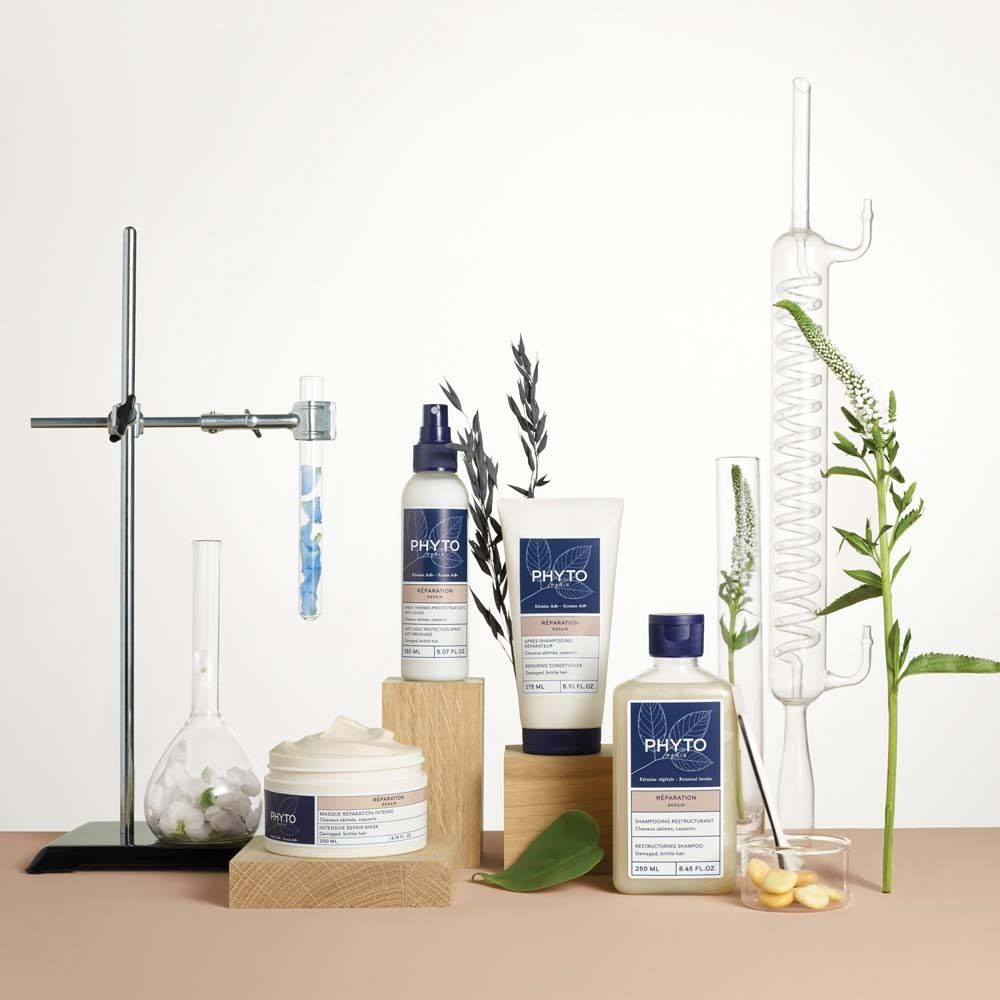 Produkt-Arrangement mit Shampoo-Flasche, Creme, Spray und Tube. Auf Holzblöcken, neben Laborutensilien und Pflanzen.