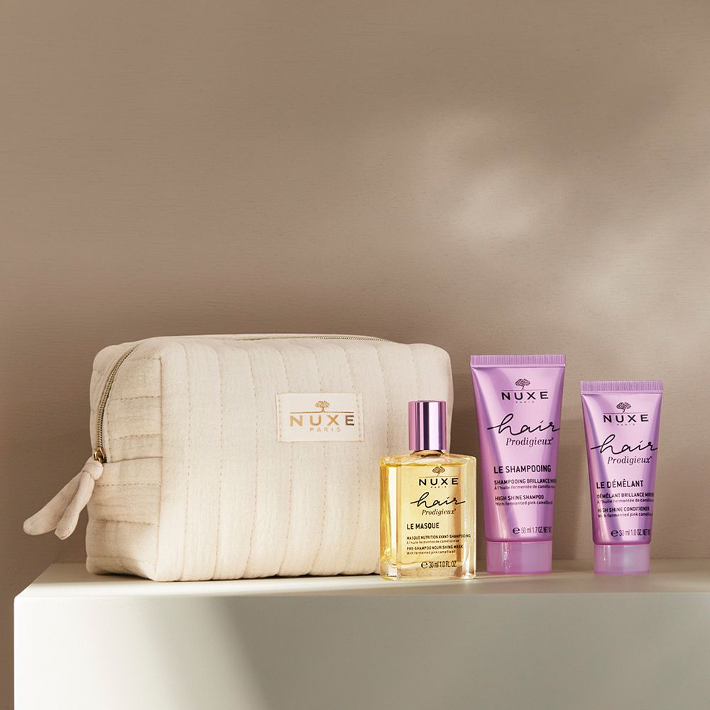 Trousse de toilette beige avec trois produits capillaires. Flacon et deux tubes. Inscription : NUXE, Hair Prodigieux. Sur surface blanche.