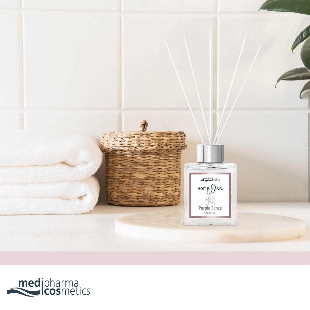 Diffuseur d'ambiance avec bâtonnets sur un plateau. Flacon avec bouchon argenté et étiquette blanche. Serviettes et panier en arrière-plan.