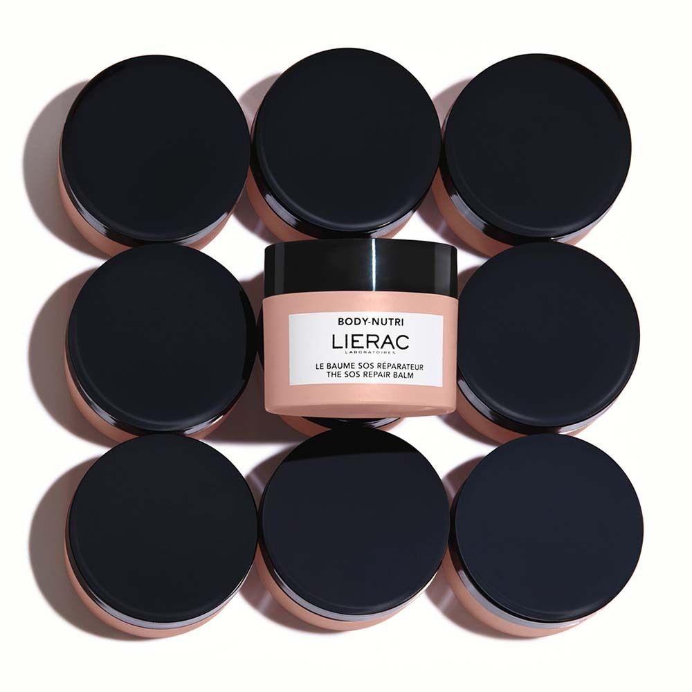 Huit pots à couvercles noirs entourent un pot avec une étiquette blanche. Inscription : LIERAC, LE BAUME SOS RÉPARATEUR, THE SOS REPAIR BALM.