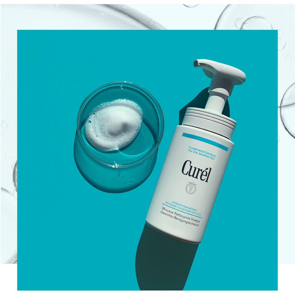 Distributeur blanc avec mousse dans un verre. Inscription : Curél, Mousse Nettoyante Visage. Fond bleu.