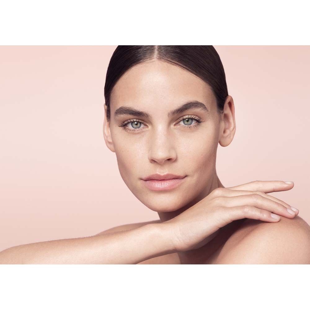 Portrait d'une femme à la peau nette. Elle a les yeux bleus et une main touche sa joue.