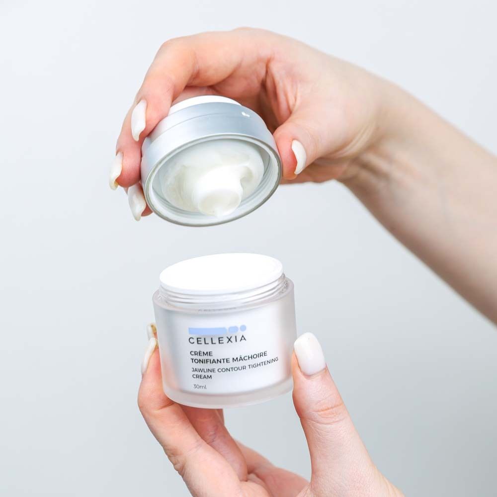 Hände halten einen Creme-Tiegel mit geöffnetem Deckel. Creme sichtbar. Aufschrift: Cellexia, Crème Tonifiante Mâchoire, 30ml.