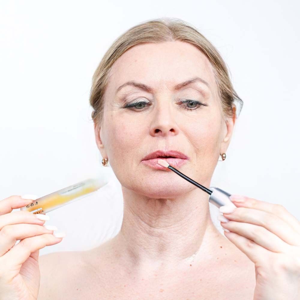 Frau hält Fläschchen und Applikator an ihre Lippen. Produkt sichtbar.