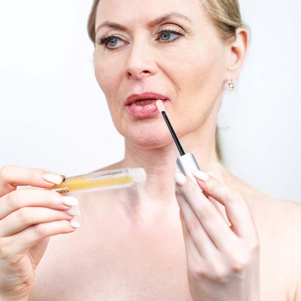 Frau hält Fläschchen und Applikator an ihre Lippen. Produkt sichtbar.