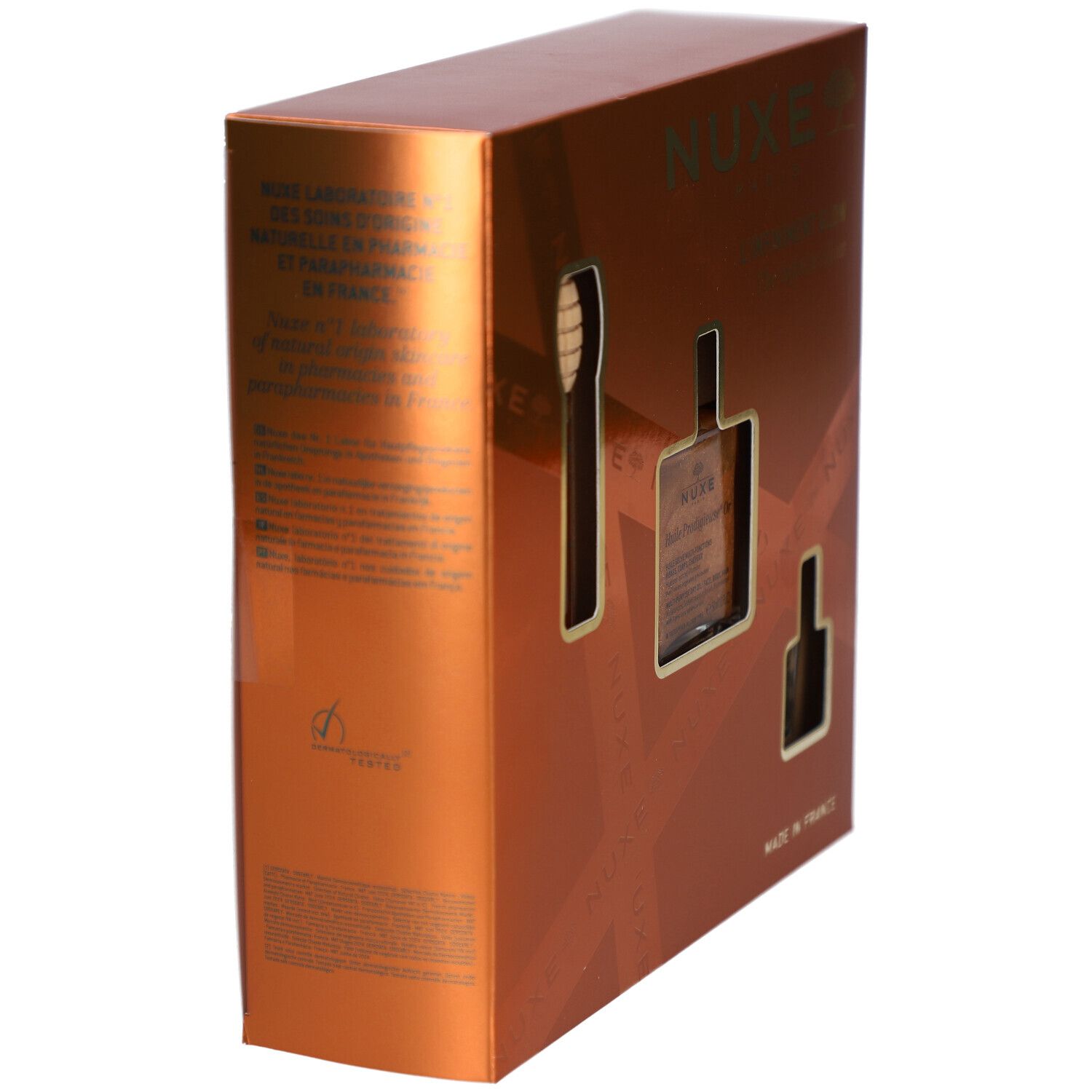 Coffret cadeau doré avec découpes pour produits. Texte : NUXE, "Made in France". Vue latérale.
