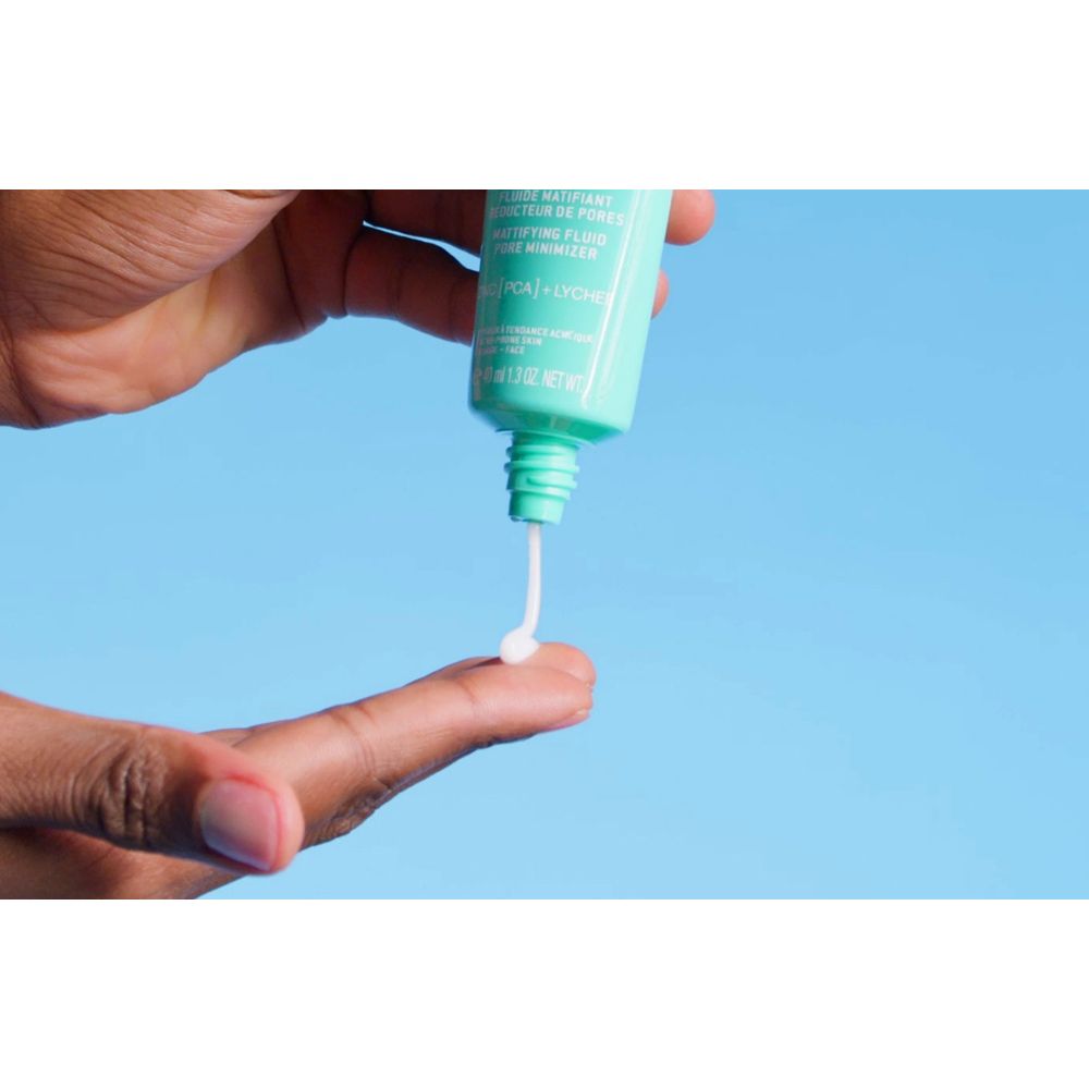 Main pressant une petite quantité de fluide d'un tube turquoise. Le fluide est blanc.