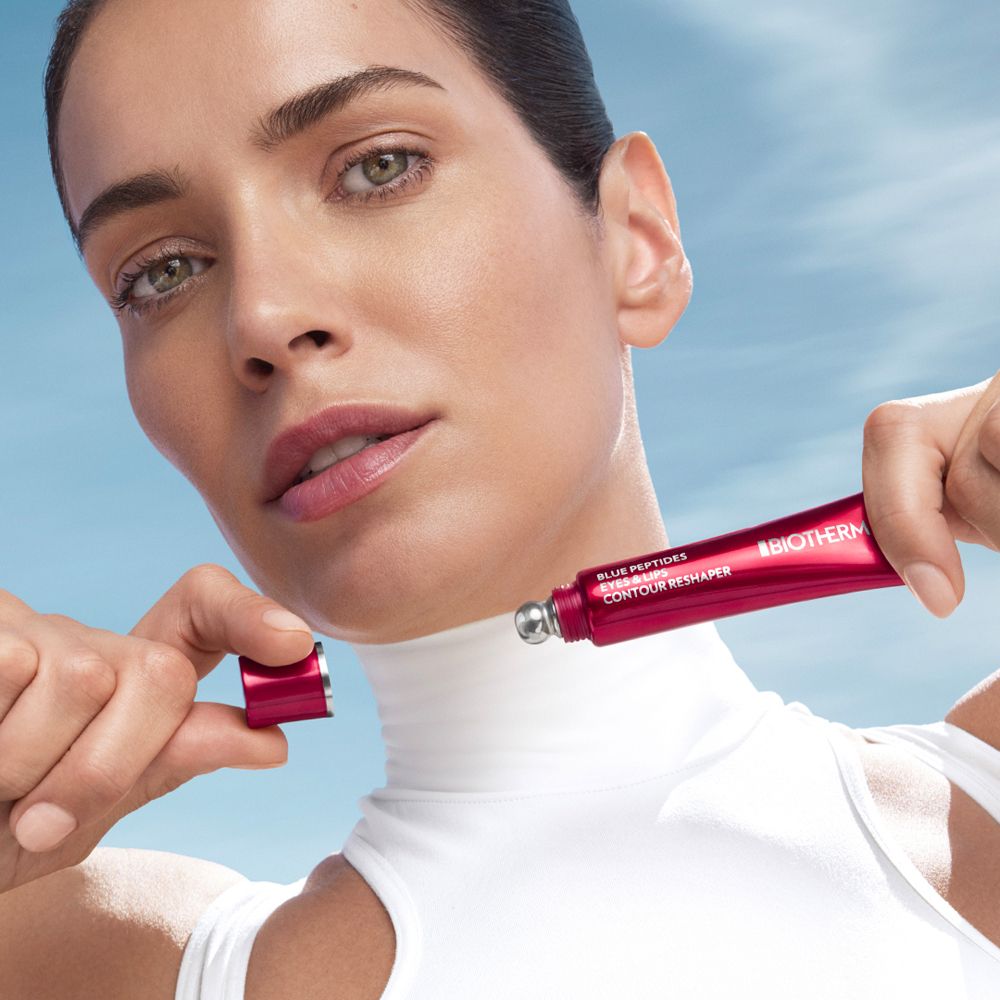 Femme tenant un tube rouge. BIOTHERM Blue Peptides Eyes & Lips Reshaper. L'applicateur est visible.