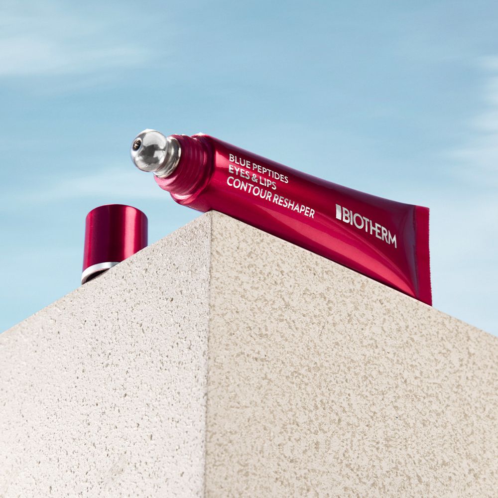 Tube rouge avec applicateur. BIOTHERM Blue Peptides Eyes & Lips Reshaper. Posé sur une surface.