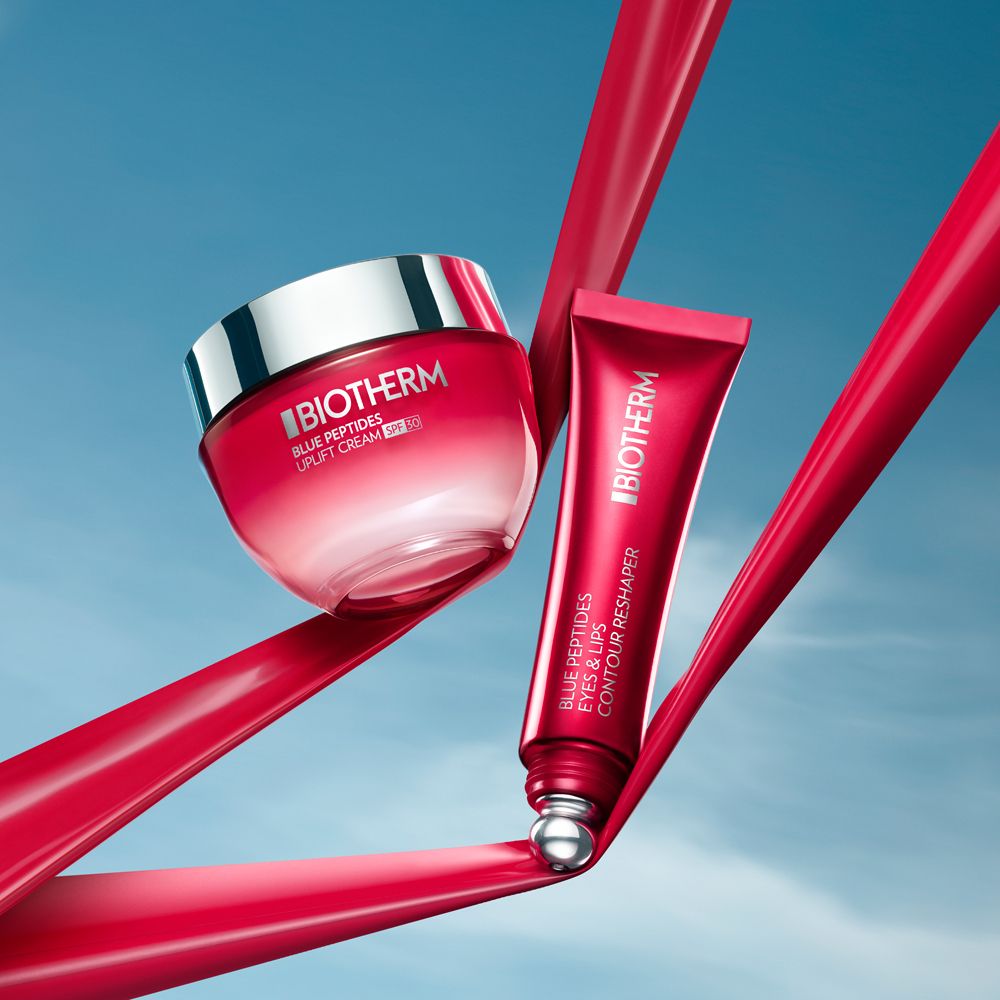 Crème et tube. BIOTHERM Blue Peptides Eyes & Lips Reshaper. Rubans rouges en arrière-plan.