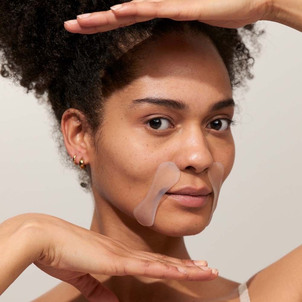 Femme avec des pads buccaux sur la lèvre supérieure. Les mains encadrent le visage. Les pads sont transparents.