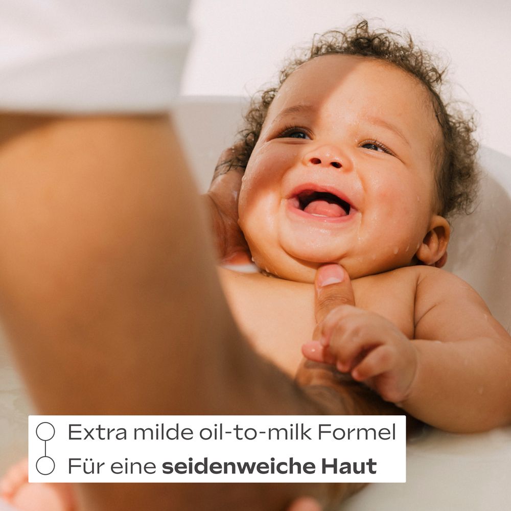 Bébé dans le bain, souriant. Texte: Formule huile-en-lait extra douce. Pour une peau douce comme de la soie.