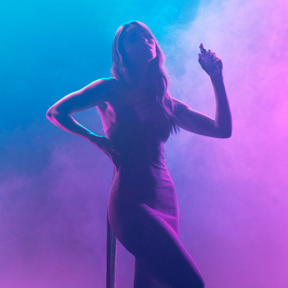 Frau mit Kleid, sprüht Duftspray. Pinker und blauer Hintergrund. Nebel.