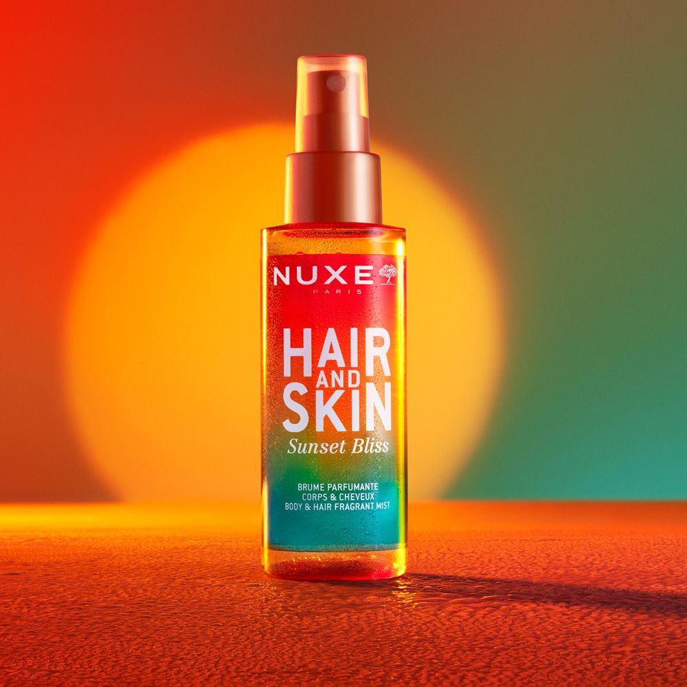NUXE® Hair and Skin Sunset Bliss Duftspray. Farbverlauf von Rot zu Grün. Sprühkopf. Text: Hair and Skin, Sunset Bliss.