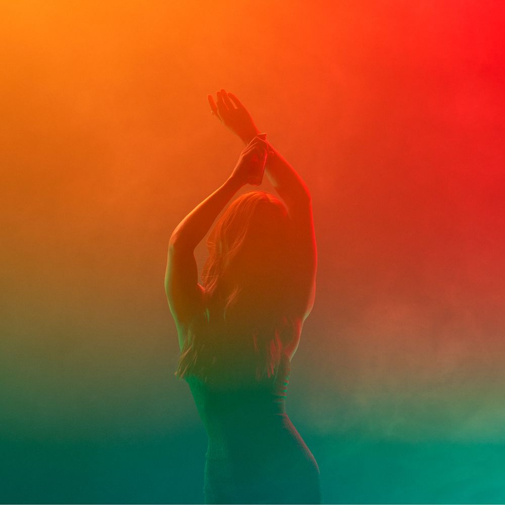 Silhouette einer Person vor farbigem Hintergrund. Arme erhoben. Hintergrundfarben: Rot, Orange, Grün.