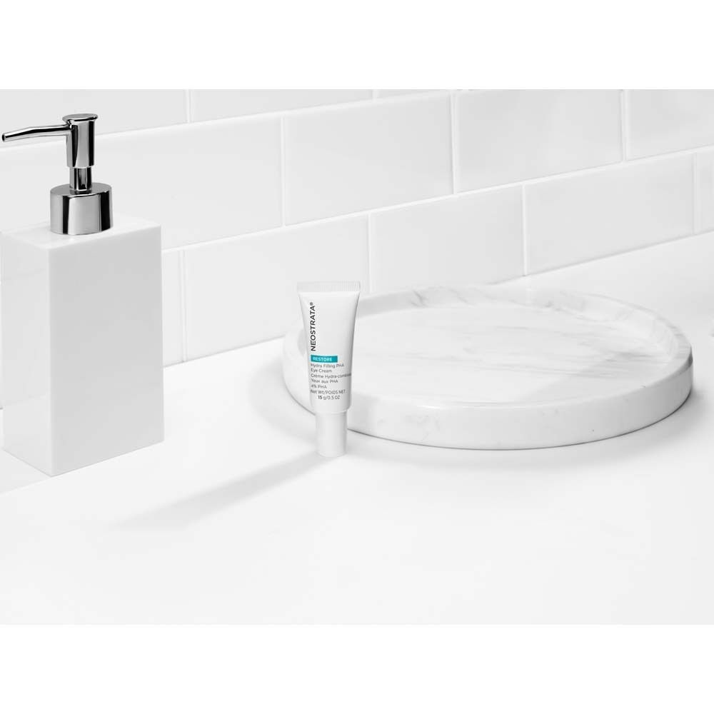 Scène de salle de bain blanche. NeoStrata Restore Eye Cream sur surface blanche. Avec distributeur de savon et plateau.