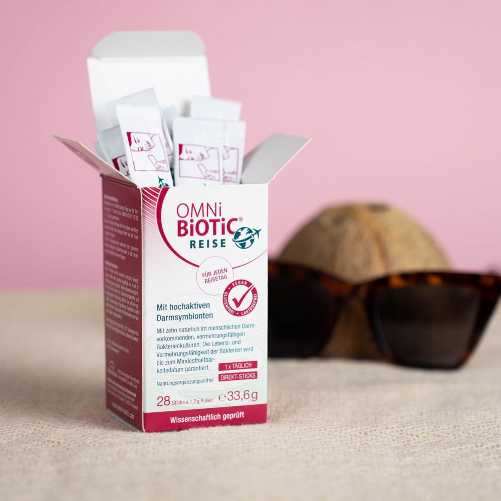 Emballage ouvert de sticks OMNi-BiOTiC REISE. Sticks visibles. Fond : noix de coco et lunettes de soleil.