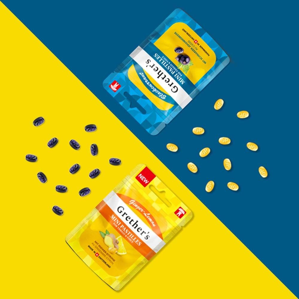 Deux paquets Grether's Mini Pastilles. Un jaune, un bleu. Pastilles à côté. Inscription : Ginger-Lemon et Myrtille.