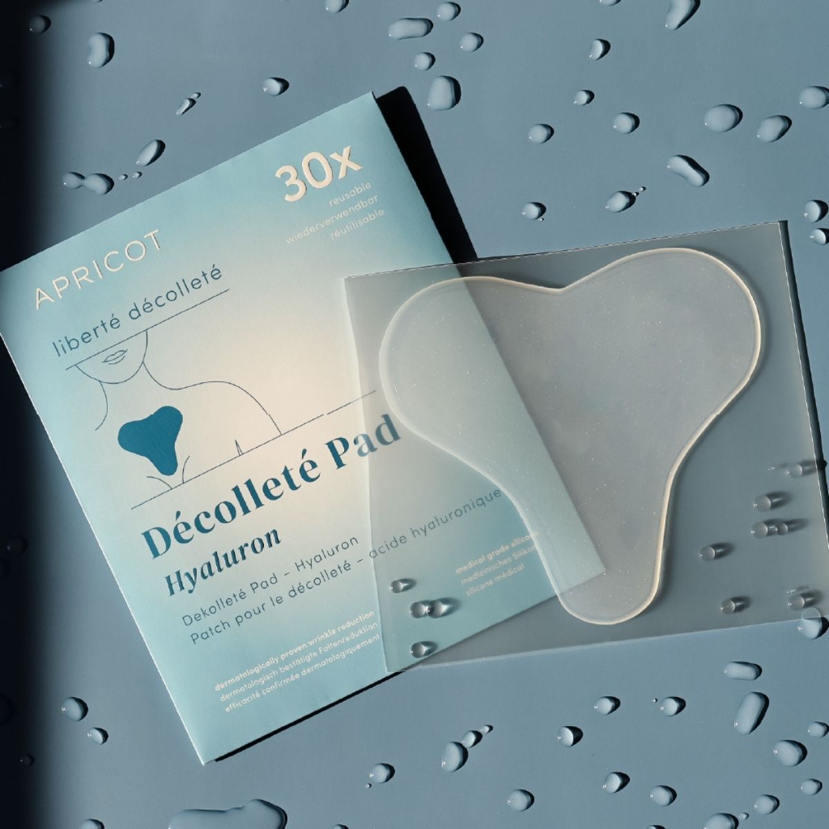 Verpackung und ein Dekolleté-Pad mit Hyaluron auf nassem Untergrund.