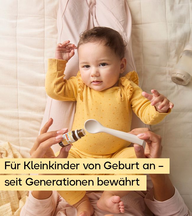 Baby in gelbem Strampler erhält Tropfen aus einer kleinen Flasche auf einem Löffel.
