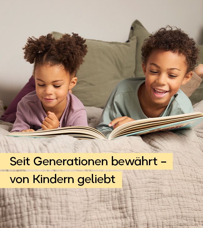 Zwei Kinder liegen auf einem Bett und lesen ein Buch. Der Junge lächelt, das Mädchen schaut auf das Buch.