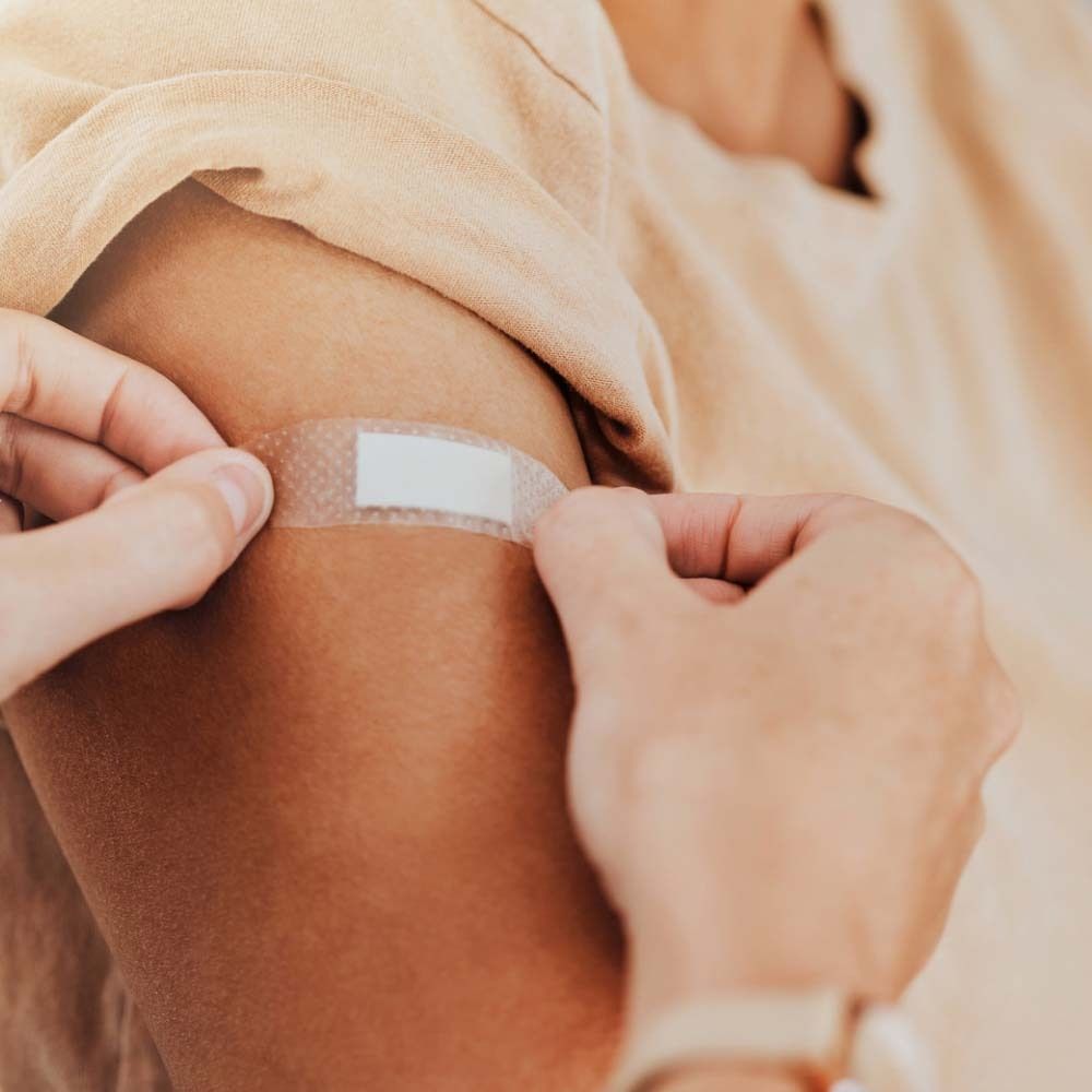 Person klebt transparentes Pflaster auf Arm. Pflaster ist rechteckig und transparent.