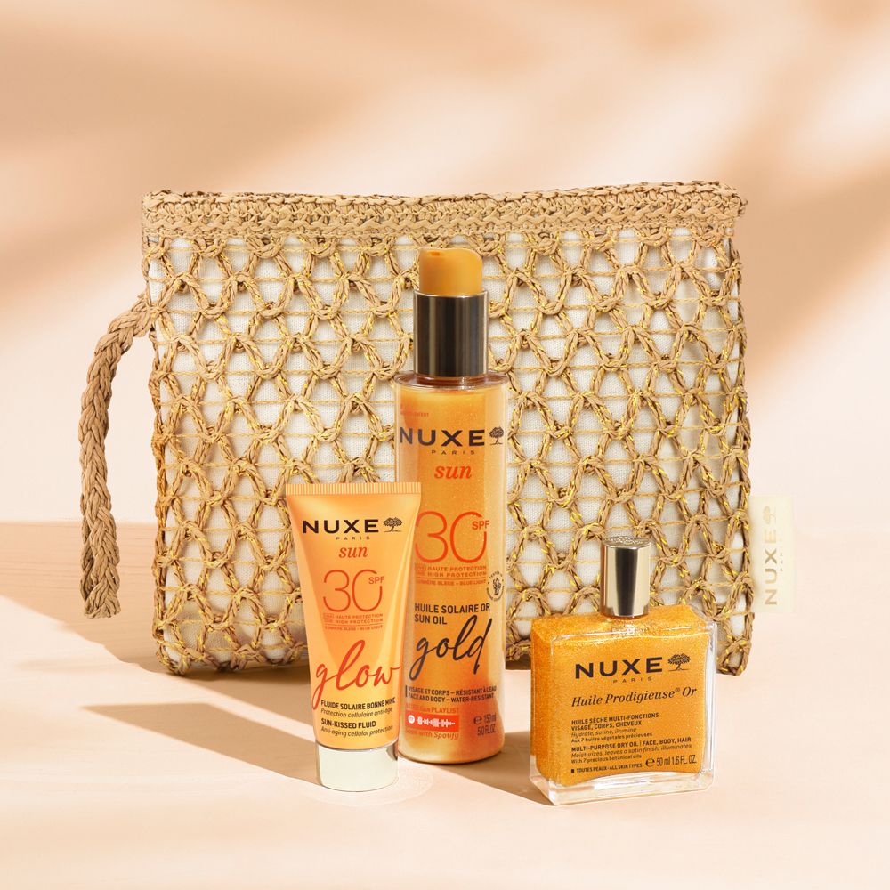 Ensemble avec huile solaire, crème solaire et huile dans une pochette beige. Produits avec étiquettes orange. Logo NUXE visible.