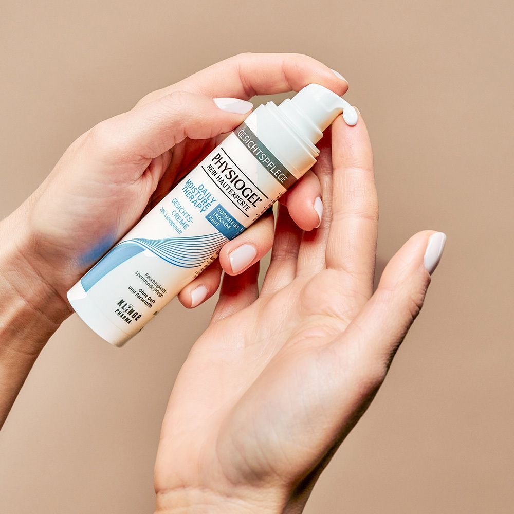 Mains tenant un tube de crème PHYSIOGEL Daily Moisture Therapy. Crème pressée.