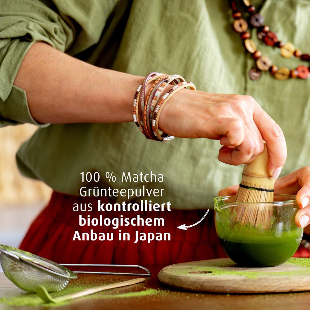 Eine Person bereitet mit einem Bambusbesen Matcha in einer Schale zu. Text: 100% Matcha Grünteepulver aus biologischem Anbau.