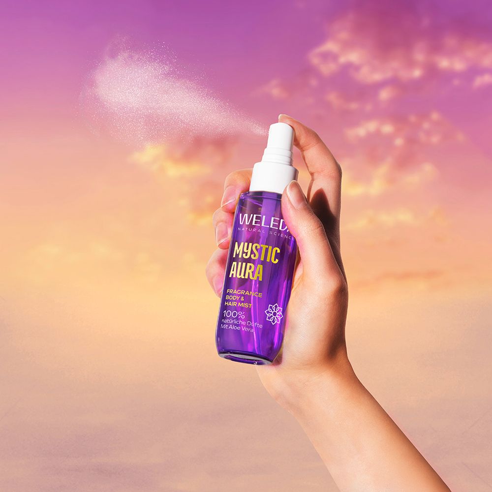 Hand sprüht lila Flasche mit gelbem Deckel. Text: WELEDA MYSTIC AURA, Fragrance Body & Hair Mist.