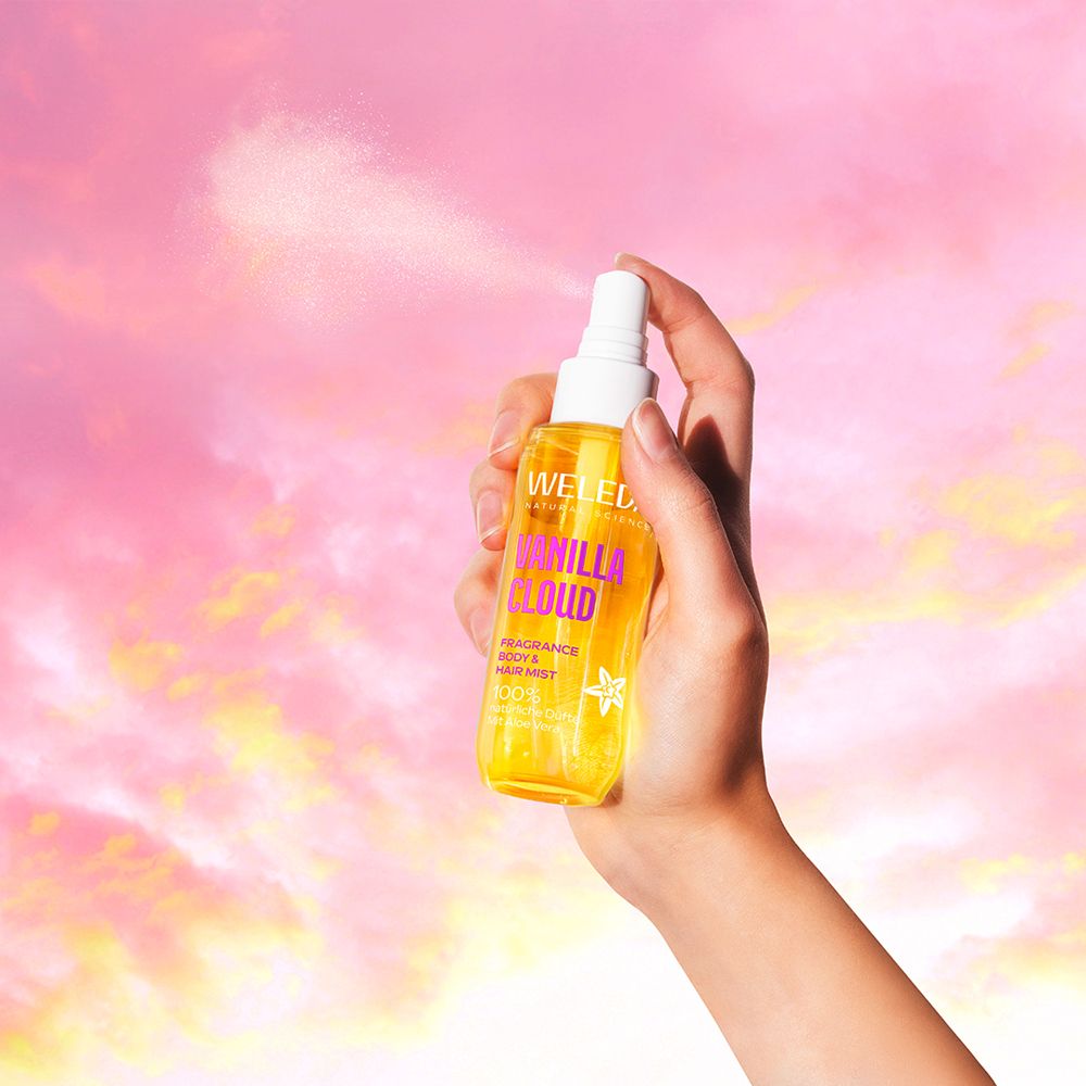 Hand sprüht Weleda Vanilla Cloud Body & Hair Mist. Gelbe Flasche mit pinkfarbenem Deckel.