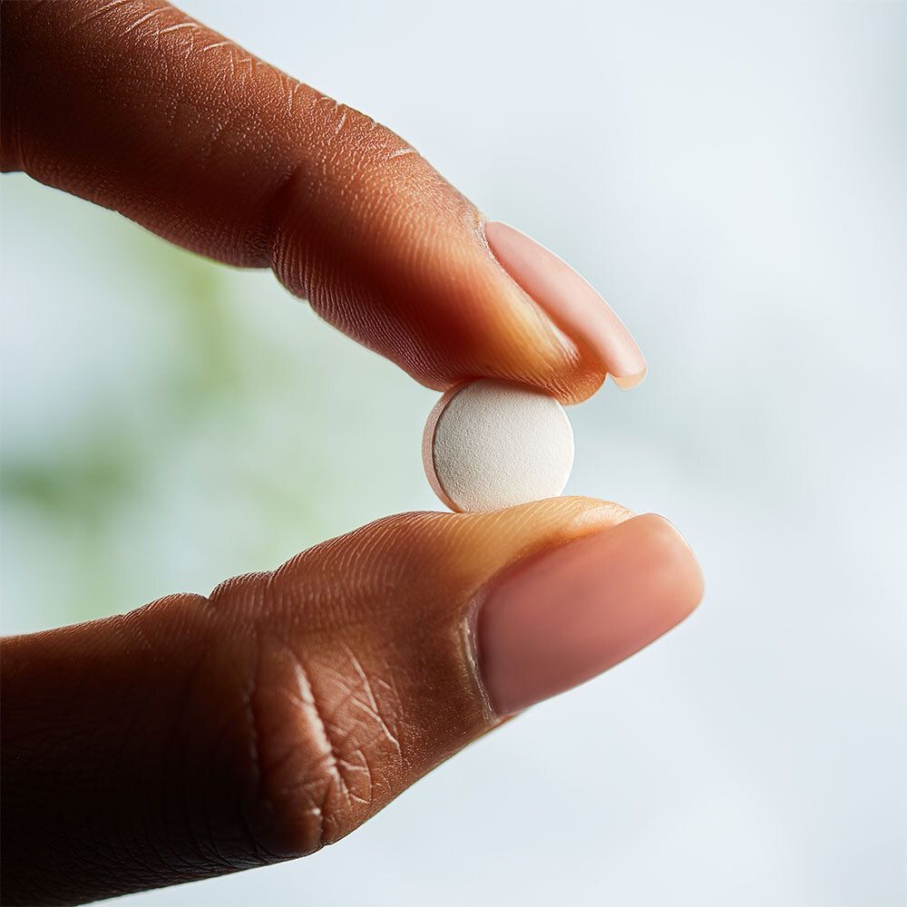 Une main tient un comprimé blanc entre le pouce et l'index.