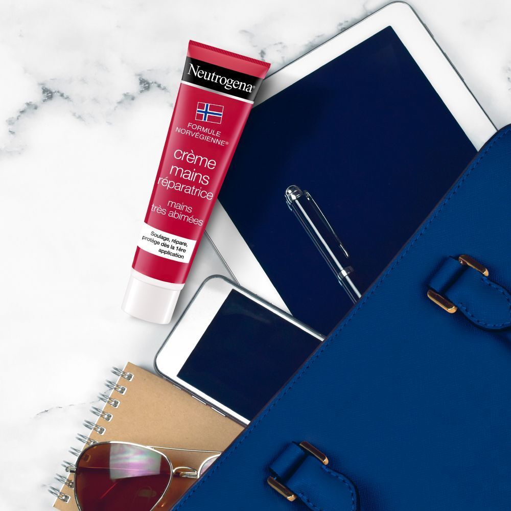 Tube de crème pour les mains à côté d'une tablette, d'un téléphone, de lunettes et d'un carnet dans un sac.