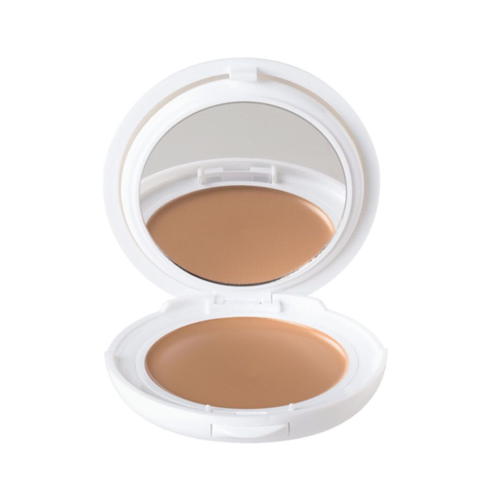 Fond de teint compact ouvert. Boîtier blanc avec miroir. Produit de maquillage beige clair visible.