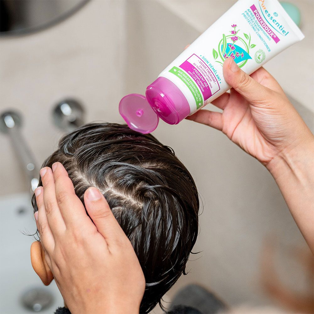 Person gibt Produkt aus einer Tube auf den Kopf eines Kindes. Tube mit lila Verschluss. Aufschrift: POUXDOUX®.