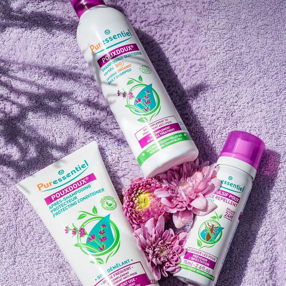 Produkt-Ensemble: Tube, Shampoo, Spray. Alle mit POUXDOUX®-Logo. Auf lila Untergrund. Blumen.