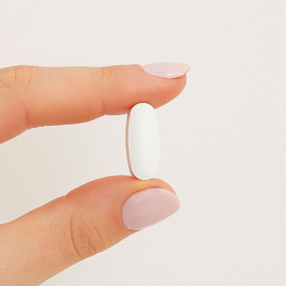 Un comprimé blanc ovale, tenu entre deux doigts.